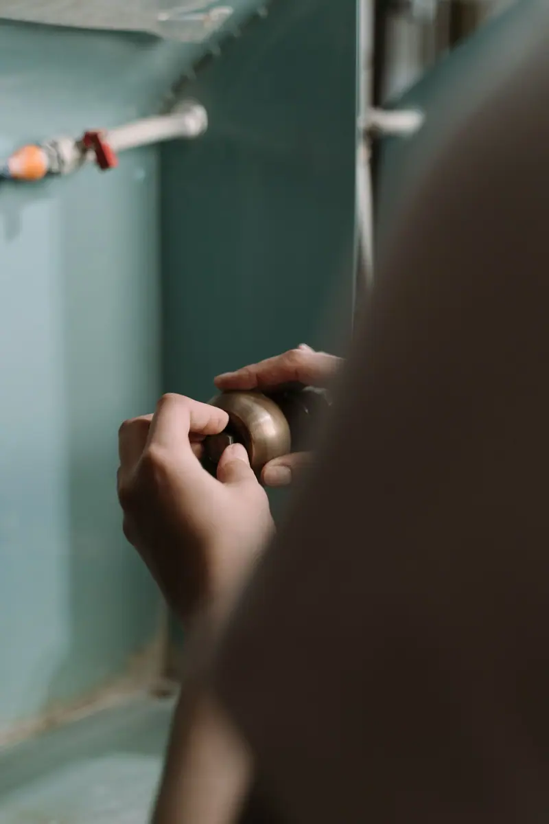 Hands loosening a drain pipe under a kitchen sink
